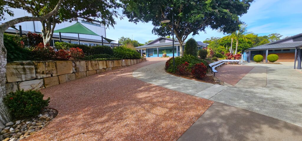 Beautifully maintained school pathway with clean, vibrant aggregate concrete, surrounded by lush landscaping and modern school buildings, showcasing our commercial cleaning services.