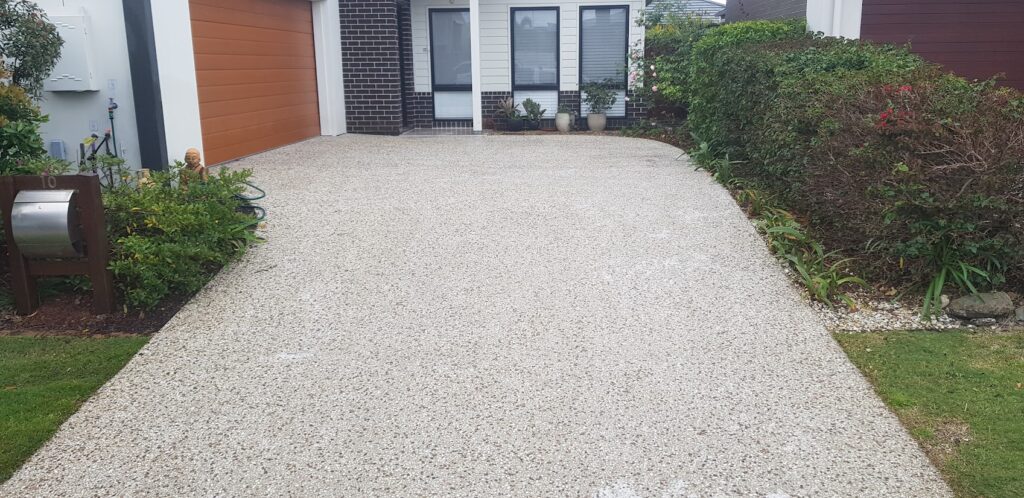 Spotless residential driveway after professional pressure cleaning, showcasing a clean and bright surface surrounded by well-maintained garden beds and a modern home exterior.